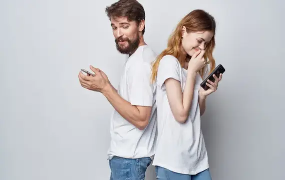 Мужчина с бородой и рыжеволосая девушка со смартфонами стоят спина к спине