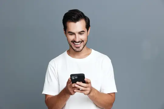Улыбающийся темноволосый мужчина в белой футболке смотрит в смартфон