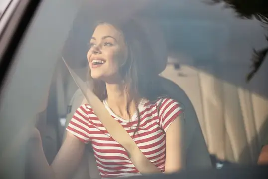 Улыбающаяся девушка в полосатой футболке за рулём автомобиля