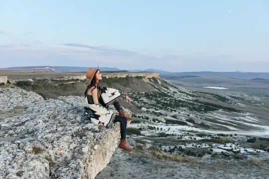 Девушка в шляпе сидит на скале над горной долиной