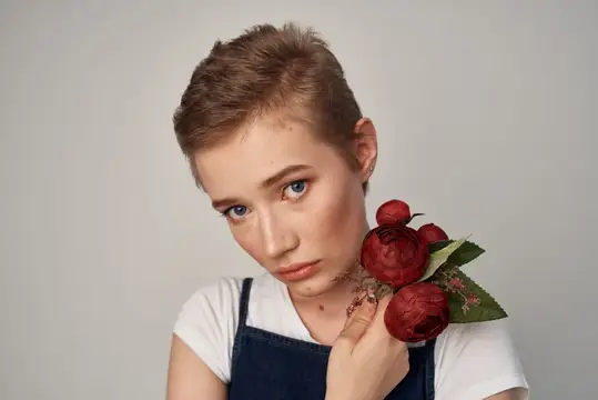 Стриженая девушка с красными розами у лица на сером фоне