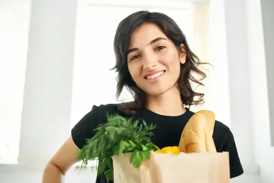 Улыбающаяся темноволосая девушка с бумажным пакетом продуктов
