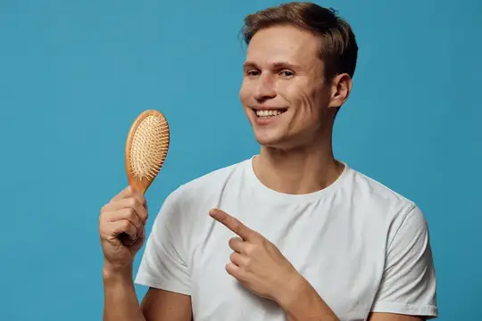 Улыбающийся парень в белой футболке показывает на деревянную расчёску