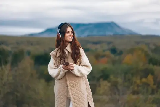 Улыбающаяся девушка в наушниках слушает музыку на фоне осенних гор