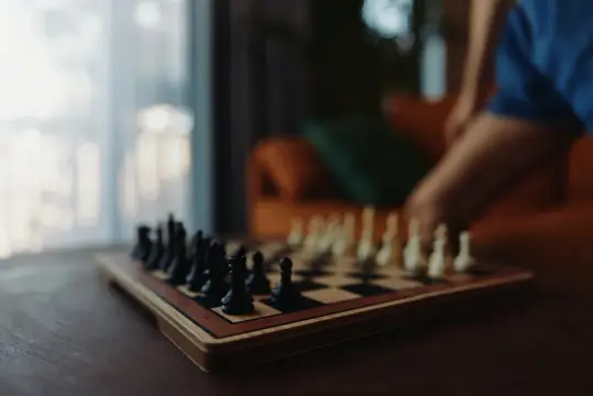 Шахматная доска с фигурами на столе и рука игрока на заднем плане