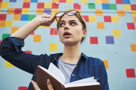 Молодая женщина с книгой поправляет очки на фоне цветной стены