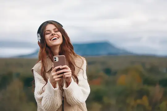 Улыбающаяся девушка в наушниках со смартфоном на фоне гор