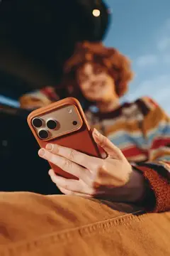 Рыжеволосая девушка в свитере смотрит в смартфон на улице