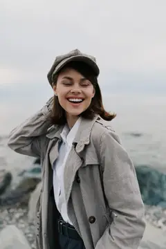 Смеющаяся девушка в кепке и плаще на берегу моря