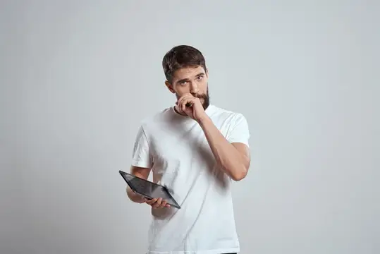 Задумчивый бородатый мужчина с планшетом на сером фоне