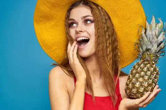 Улыбающаяся девушка в жёлтой шляпе с ананасом на синем фоне