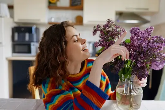 Молодая женщина с сиренью в вазе на кухне