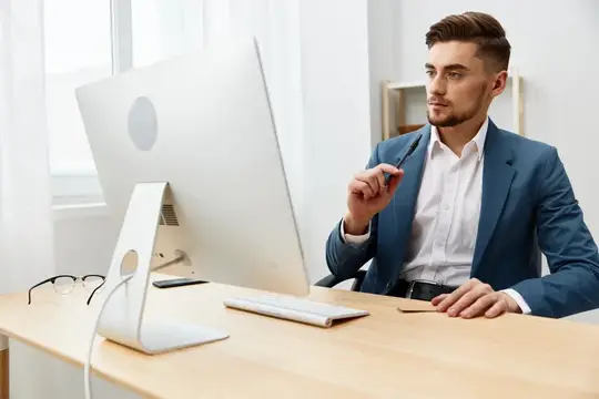 Молодой мужчина в синем пиджаке работает за компьютером в офисе