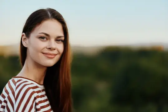 Молодая темноволосая женщина с лёгкой улыбкой на фоне зелёного пейзажа
