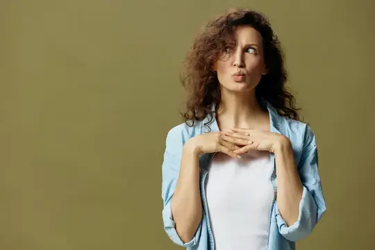 Кудрявая женщина в голубой рубашке задумчиво смотрит в сторону
