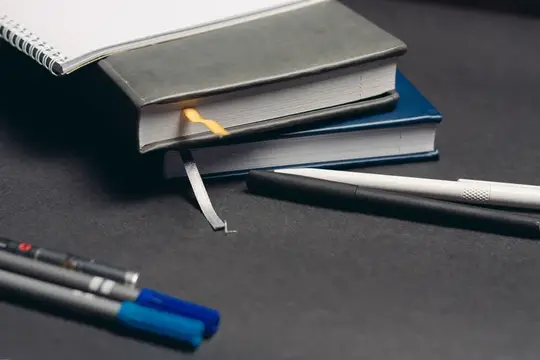 Стопка книг с закладками и ручки на тёмном столе