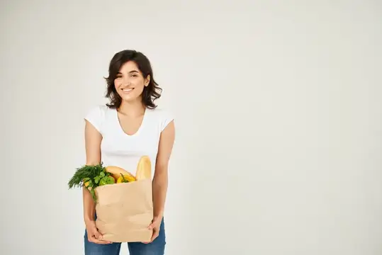 Весёлая брюнетка в белой футболке с сумкой для продуктов
