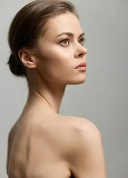 Молодая женщина с гладкой причёской смотрит в профиль на сером фоне