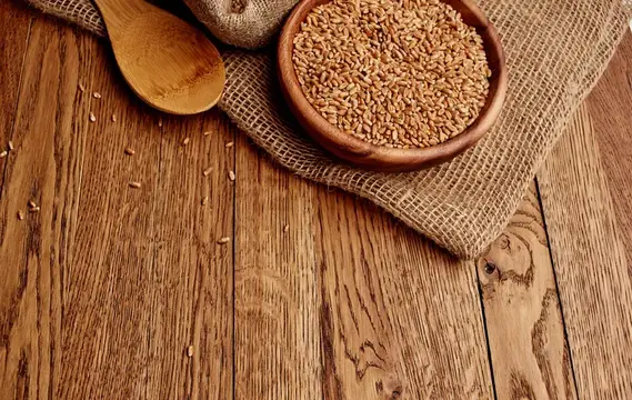 Глиняная миска с пшеничными зёрнами и деревянная ложка на мешковине