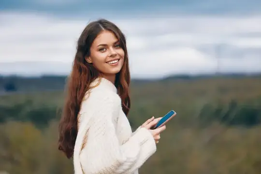 Улыбающаяся девушка с телефоном на фоне осеннего поля