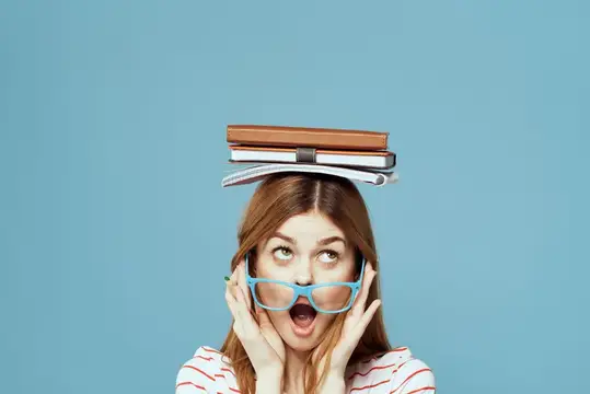 Удивлённая девушка с книгами на голове в голубых очках