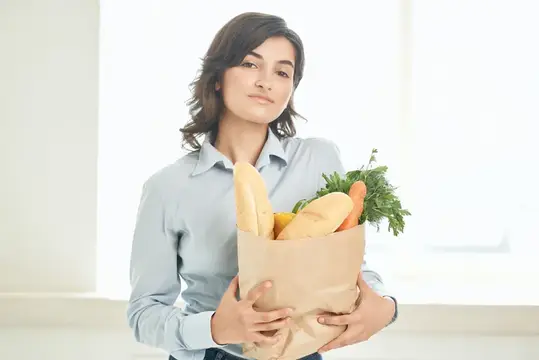 Молодая женщина с бумажным пакетом свежих продуктов у окна