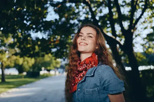 Улыбающаяся девушка с длинными волосами в красном платке на прогулке в парке