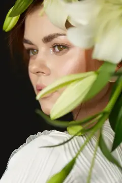 Потрясающая женщина с зелеными глазами и длинными каштановыми волосами в обрамлении белых лилий, излучающая элегантность и естественную красоту в изысканной цветочной обстановке, идеально подходит…