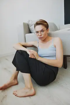 Молодая женщина в очках сидит на полу у дивана