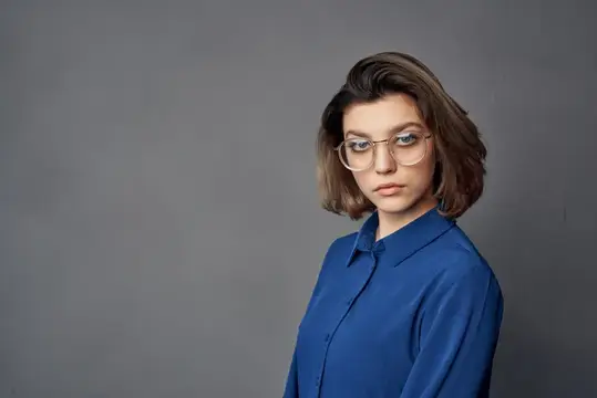 Молодая женщина в очках и синей рубашке на сером фоне
