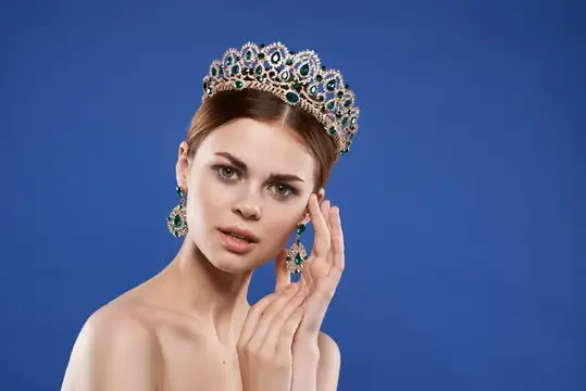 Молодая женщина в роскошной короне с изумрудами на синем фоне