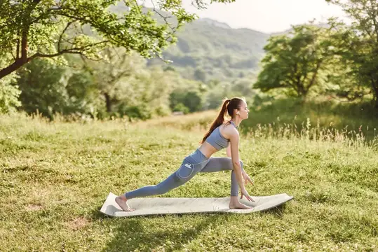 Красивая девушка занимается йогой на коврике в мирном зеленом пейзаже, что иллюстрирует здоровье, хорошее самочувствие и фитнес на свежем воздухе