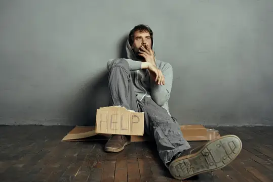 Бородатый бомж сидит на полу, держа табличку «Help»