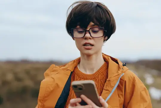 Молодой человек в очках с телефоном на фоне осеннего поля