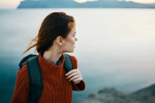 Молодая женщина с рюкзаком смотрит на горное озеро