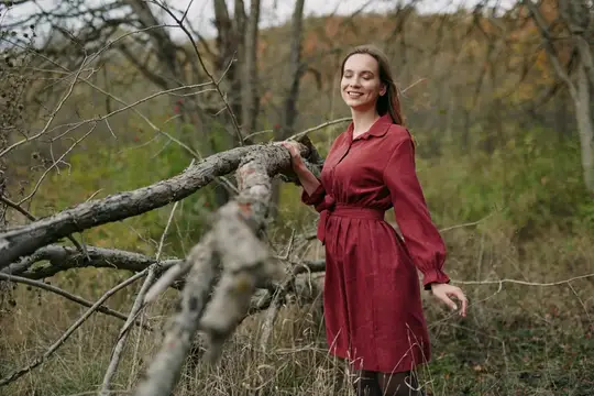 Улыбающаяся женщина в бордовом платье у поваленного дерева
