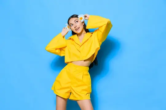 Молодая девушка в жёлтом костюме с ромашками у лица на синем фоне