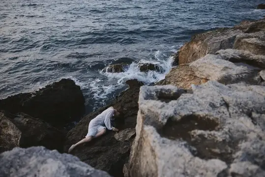 Женщина лежит на прибрежных камнях у бурного моря