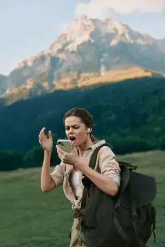 Удивлённая туристка с рюкзаком смотрит в телефон на фоне гор