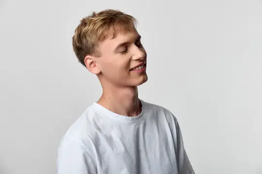Молодой человек с мягкой улыбкой, в белой рубашке на нейтральном студийном фоне, излучает доступное тепло и непринужденность, идеально подходит для брендинга, рекламы или редакционных стоковых…