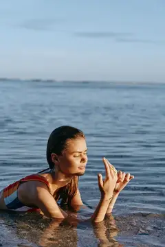 Молодая женщина с закрытыми глазами молится, стоя в воде на закате