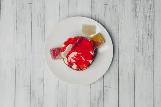 Десерт с ягодным соусом и кусочками мармелада на белой тарелке