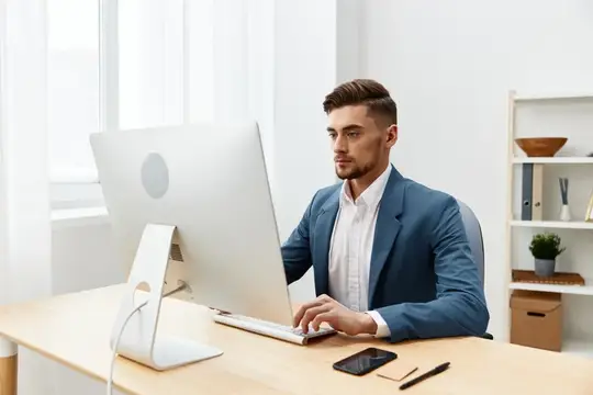 Молодой мужчина в синем пиджаке работает за компьютером в светлом офисе