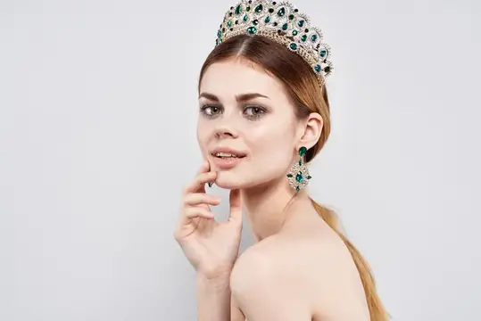Молодая женщина в роскошной короне с изумрудами на светлом фоне