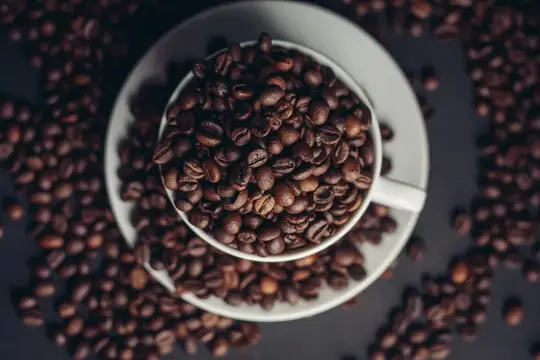 Белая чашка с кофейными зёрнами на тёмном фоне
