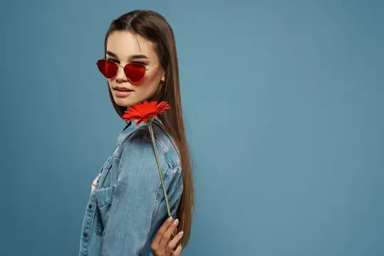 Молодая девушка в красных очках с цветком за спиной на синем фоне