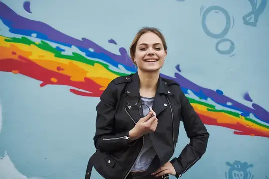 Улыбающаяся девушка в кожаной куртке на фоне радужного граффити