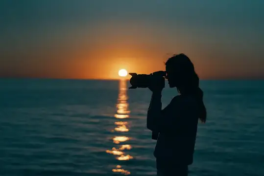 Силуэт девушки с фотоаппаратом на закате у моря