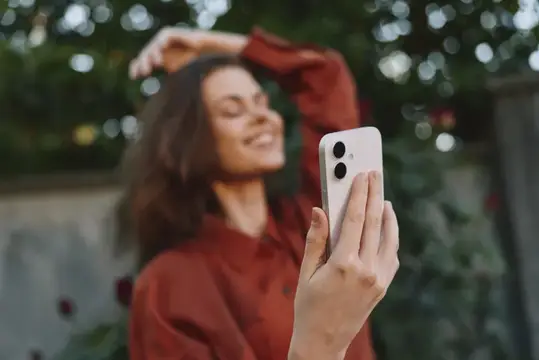 Улыбающаяся темноволосая женщина делает селфи на смартфон в саду