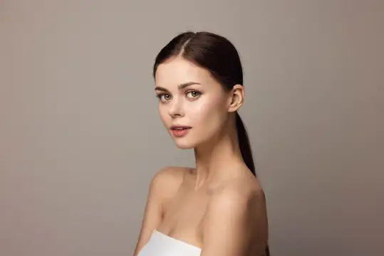 Молодая темноволосая женщина с гладкой причёской на сером фоне